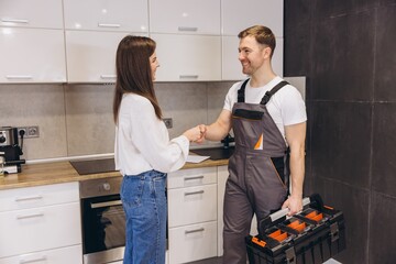 Plumber shaking hands with woman after finishing work in kitchen