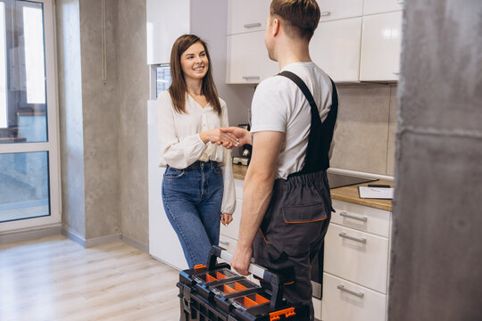 Plumber shaking hands with woman after finishing work in kitchen
