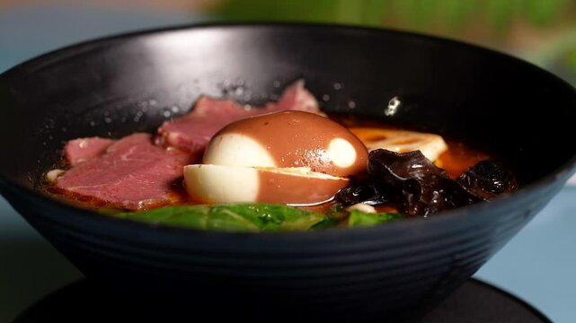 Full view of ramen bowl showcasing soy egg, tender beef slices, mushrooms, and fresh spinach leaves.