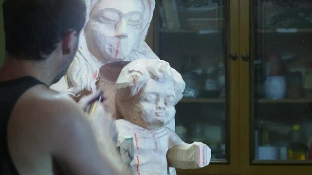 Skilled strong caucasian sculptor carving wooden virgin mary religious statue with mallet and chisel in workshop, showcasing creativity and craftsmanship in close up shot, slow motion