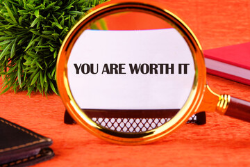 YOU ARE WORTH IT words focuses through a magnifying glass on a business card on an orange background