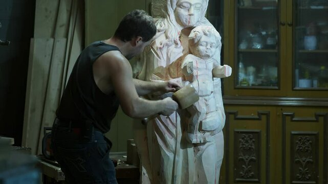 Skilled strong caucasian sculptor carving wooden virgin mary religious statue with mallet and chisel in workshop, showcasing creativity and craftsmanship in close up shot, slow motion