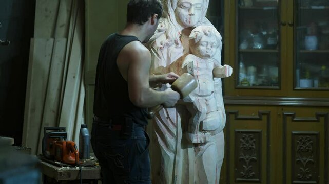 Skilled strong caucasian sculptor carving wooden virgin mary religious statue with mallet and chisel in workshop, showcasing creativity and craftsmanship in close up shot, slow motion