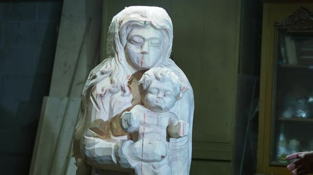 Skilled strong caucasian sculptor carving wooden virgin mary religious statue with mallet and chisel in workshop, showcasing creativity and craftsmanship in close up shot, slow motion