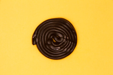 Black licorice wheel creates perfect spiral pattern on bright yellow background. Minimalist food photography showcasing confectionery design with bold color contrast.
