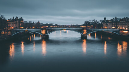 Obraz premium An illuminated bridge over a calm river at twilight.