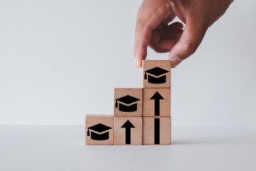 Hand stacking wooden blocks with graduation cap icons to form a staircase. Concept for higher education,step-by-step learning,professional development, continuous learning, skill improvement.