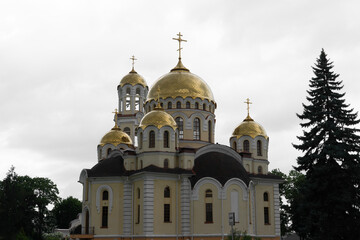 Golden domes shine under cloudy skies at an ornate Russian Orthodox church in a tranquil setting