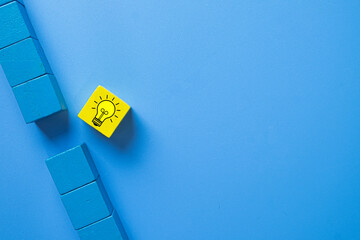 Concept for different thinking, creativity, unique solutions,finding a breakthrough,and innovative problem-solving., A yellow wooden block with a lightbulb idea icon breaks a pattern of blue blocks.