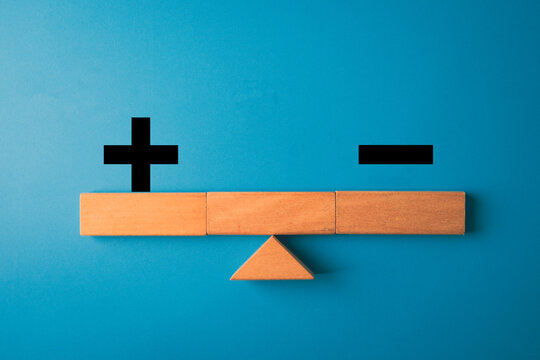 Wooden blocks forming a balance scale with plus and minus signs on blue background concept for comparison, weighing advantages,decision-making,strategic evaluation,SWOT analysis.