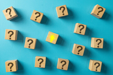 A single wooden block with a yellow lightbulb idea icon surrounded by blocks with question marks. Concept for finding a solution, problem-solving, answering questions, and creative thinking.