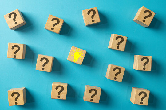A single wooden block with a yellow lightbulb idea icon surrounded by blocks with question marks. Concept for finding a solution, problem-solving, answering questions, and creative thinking. - Powered by Adobe