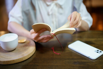 暖かい雰囲気の空間で、本を読む若い女性の手元
