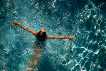 A girl in the pool, submerged in water with her arms outstretched, embracing the feeling of freedom, serenity, and weightlessness.








