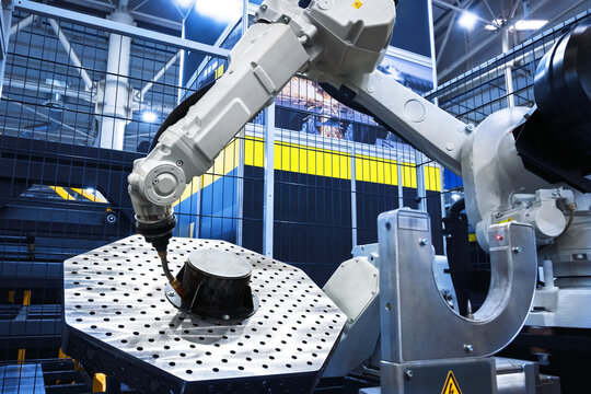 Robotic arm performs automated work on a metal part in a modern industrial factory. Manufacturing automation and technology concept. - Powered by Adobe