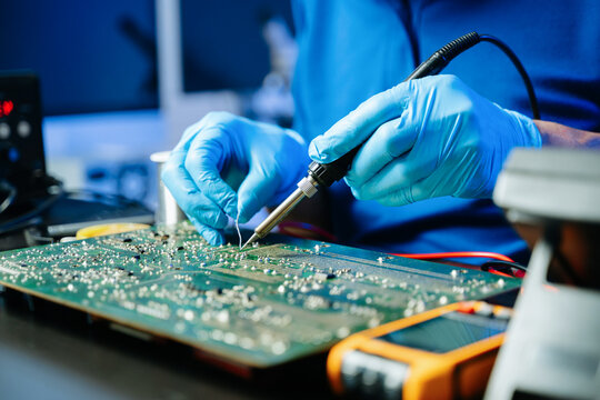 Closeup of expert soldering a green PCB board using precision tools. Ideal for electronics, circuit repair, engineering, tech