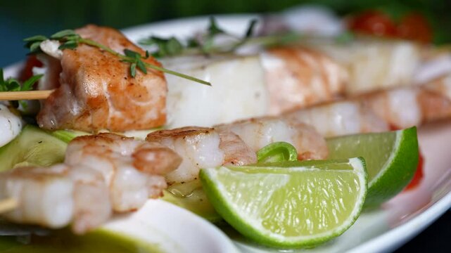 Close-up of grilled salmon, shrimp, and white fish skewers with fresh lime wedges and herbs.