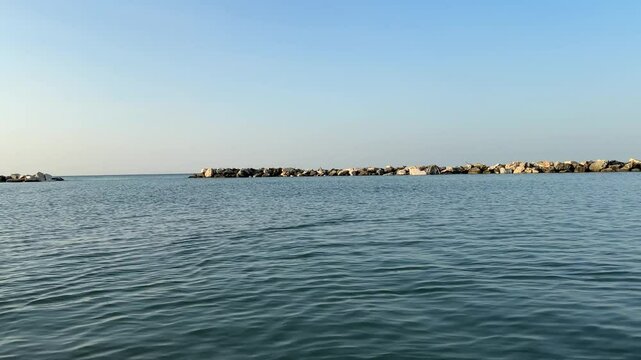 Camera panning from the port of Bellaria Igea Marina revealing the protection rocks, and a beautiful sunset reflecting on water. Peaceful moment of beauty in nature.