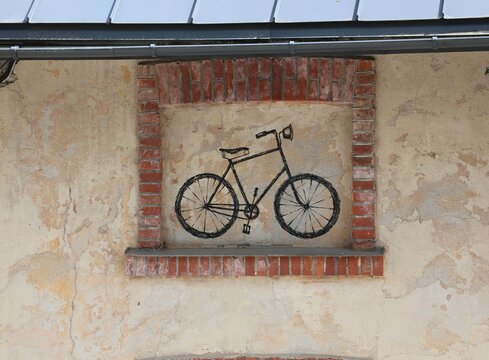 A hand-drawn black bicycle illustration framed in red bricks on a weathered plaster wall, blending rustic charm with artistic street-style detail on an aged building facade.