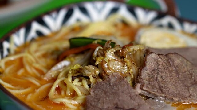 Detailed view of ramen noodles submerged in broth, with beef, napa cabbage, carrots, and peppers.
