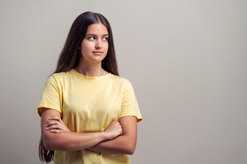 Confident teenage girl in yellow t-shirt with crossed arms standing against blank neutral background