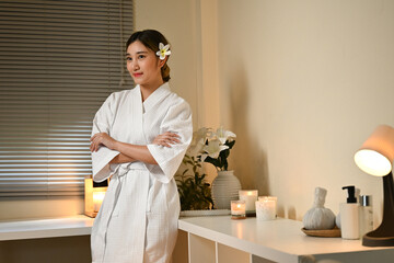 A woman in a white robe is sitting at a spa with a pile of towels and candle. The room is dimly lit and has a calming atmosphere