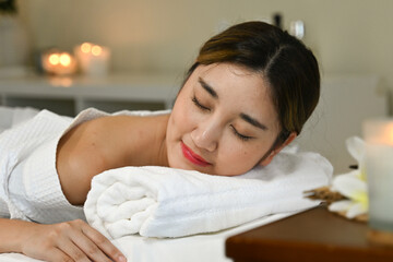 A woman is laying on a massage table with a white robe on. She is smiling and she is relaxed