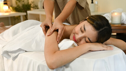 Fototapeta premium A woman is getting a massage from a massage therapist. She is smiling and relaxed. The massage table is covered with a white towel