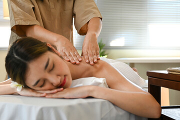 A woman is getting a massage from a massage therapist.The woman is smiling and she is enjoying the massage. a massage therapist is massaging her back