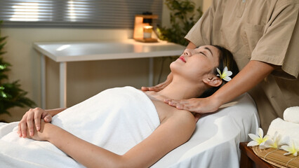 A woman is lying on a massage bed and a masseuse is massaging her shoulders. The atmosphere is...