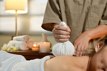professional masseur is making hot herbal ball treatment on woman in serene spa setting, promoting relaxation and wellness