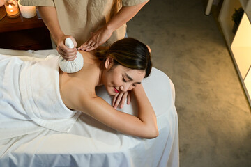 professional masseur is making hot herbal ball treatment on woman in serene spa setting, promoting relaxation and wellness