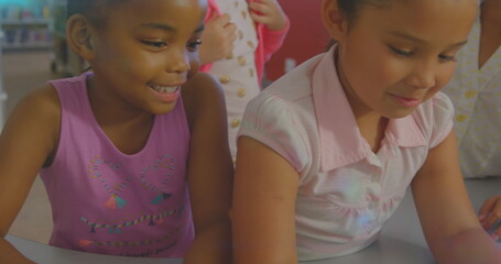 Image of glowing light over diverse school children using laptop in classroom