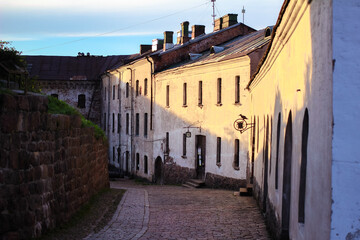 Fototapeta premium Sunset view of a street near Vyborg Castle in Russia, with old buildings and stone walls. Concept of medieval European architecture, historic towns, and atmospheric heritage streets