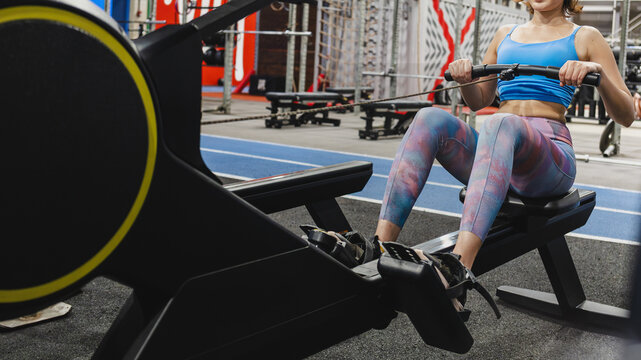 Movement: Fit and focused young woman in sportswear working out on a rowing machine