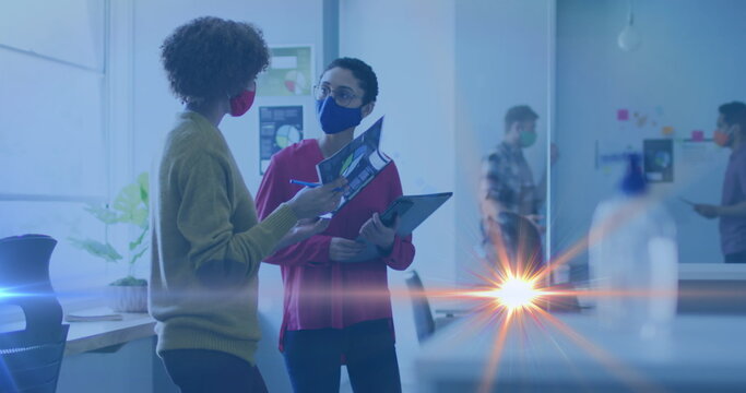 Image of light spot moving against two diverse female office colleagues discussing at office - Powered by Adobe