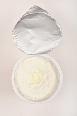 An opened white plastic container of fresh cottage cheese with a small dollop of butter or cream on top, viewed from above