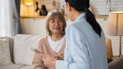 Obraz premium Asian elderly woman consulting with a doctor at home or in a nursing care setting. Medical discussion, healthcare insurance, expert advice, diagnosis support, and senior care service.