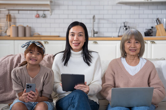 Asian three generations family with girl playing mobile phone, mother working on tablet, grandmother reading book