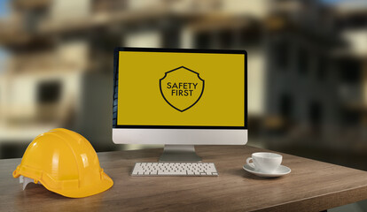 Workplace safety construction site Workstation with safety helmet, computer monitor displaying safety message, and coffee cup, emphasizing