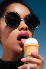 a glamorous woman with glossy pink lips licking a vanilla ice cream cone, wearing large round sunglasses