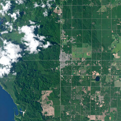 Fototapeta premium Aerial View of Town Surrounded by Lush Green Forest and Agricultural Fields