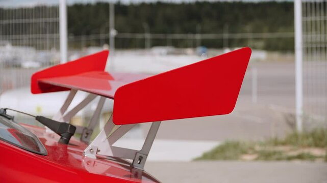 Red sports car trunk spoiler for increased downforce close up. Additional accessories for improved handling in racing and giving stylish aggressive look.