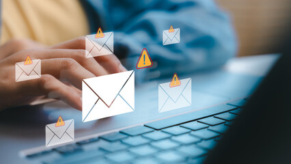 Hands typing on a laptop with warning email icons, representing phishing attacks, scam messages, and email security threats in a digital communication concept.