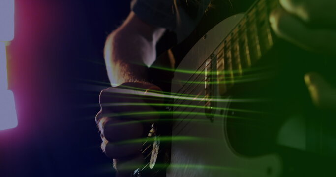 Image of green light trails over slow motion hand of musician playing electric guitar