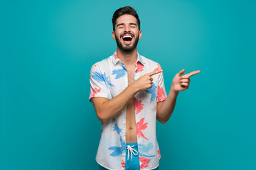 Handsome man with beard in tropical shirt pointing and laughing on turquoise background, perfect for summer promotions, travel ads, or lifestyle content
