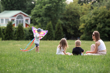 A family with three children. A mother with many children and toddlers in a summer park. Children are walking and flying a kite. Large families, family values, and leisure time with children.