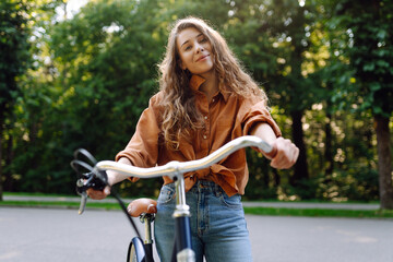 Young woman riding a bicycle in a green park. Cheerful woman enjoying weekend, bike ride at sunset. Active lifestyle. Joy, weekend concept.
