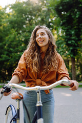 Young woman riding a bicycle in a green park. Cheerful woman enjoying weekend, bike ride at sunset....
