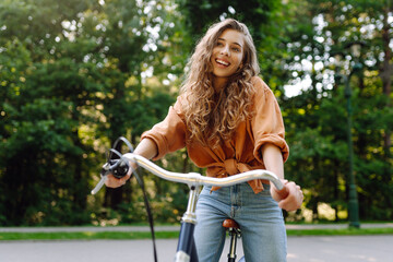 Young woman riding a bicycle in a green park. Cheerful woman enjoying weekend, bike ride at sunset....